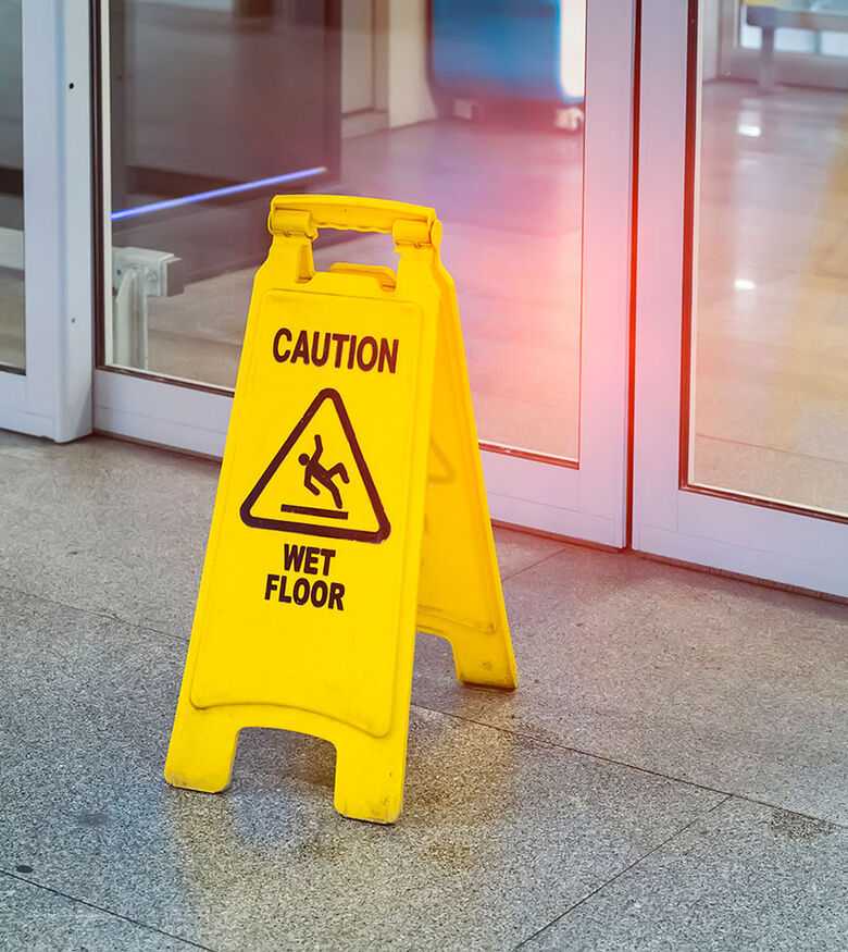 Yellow caution wet floor sign in front of sliding glass doors at an indoor facility
