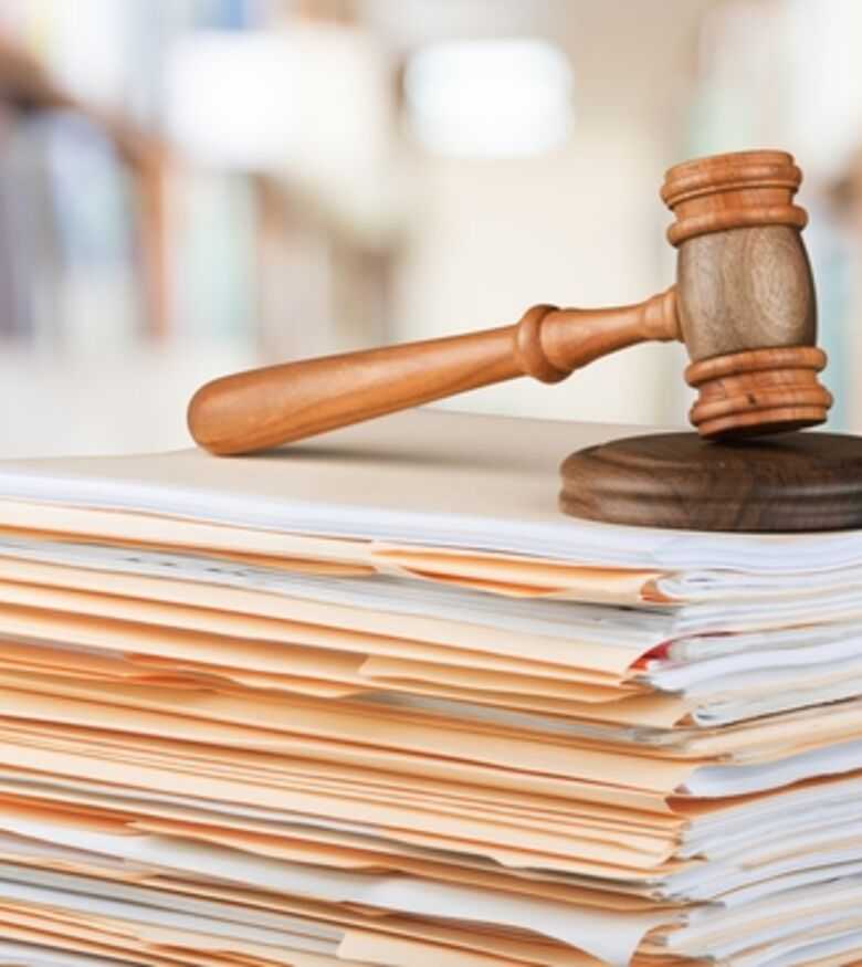 Judicial gavel on top of a large stack of legal documents with a blurred courtroom background