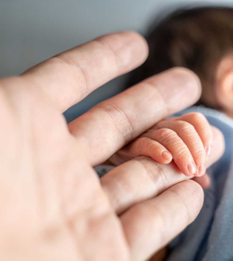 Adult hand gently holding a newborn's hand