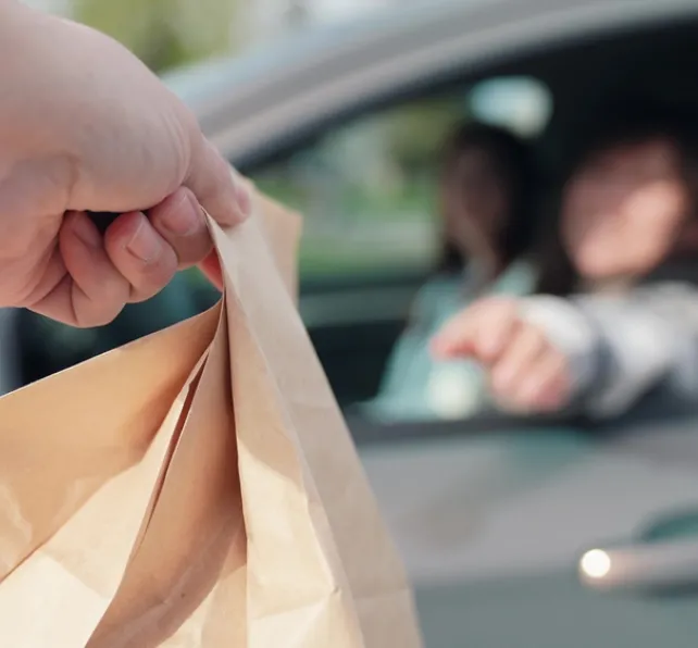 Fast food concept, delivery through auto window. Delicious meal, for travelers by auto. Woman driving, food delivery to car in package. Food for driver, passenger to eat on road. Buying food in car.