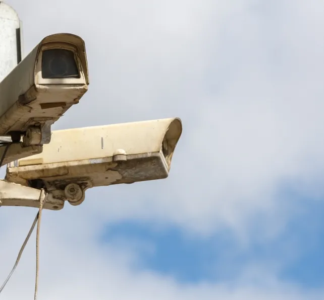 two old CCTV surveillance cameras on street pole at summer day, closeup