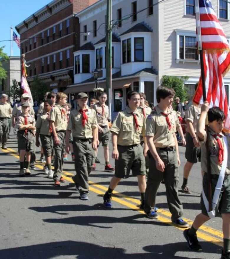 Boy Scouts marching in a parade with American flags on a sunny day