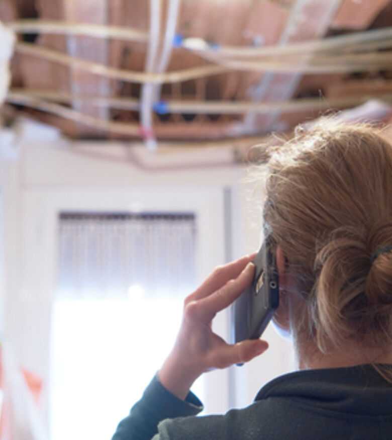 Woman on phone surveying water damage to ceiling