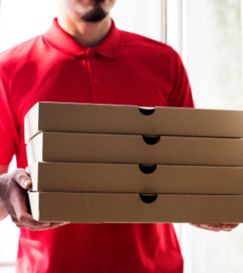 Pizza delivery person in red uniform holding a stack of pizza boxes