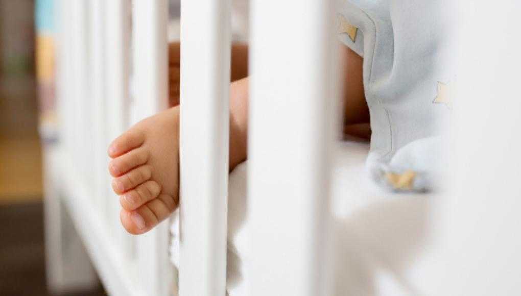 Close-up of a baby's foot sticking out between white crib slats