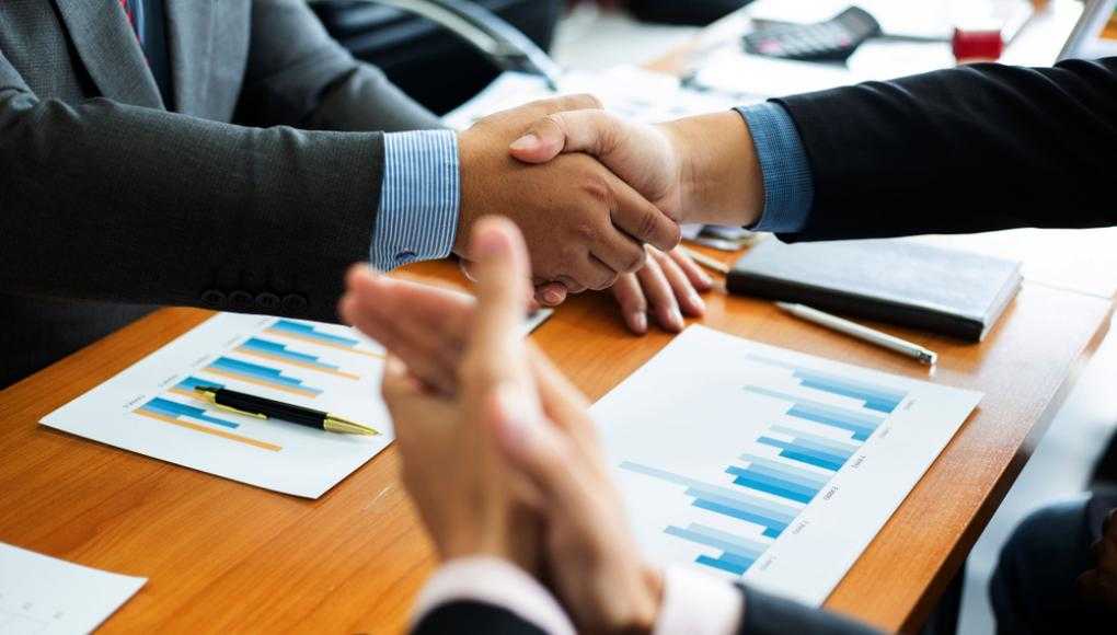 Business professionals shaking hands over a desk with financial charts, symbolizing agreement during the discovery process in legal proceedings