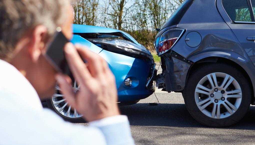 Man on phone after a car accident with visible damage to both cars.