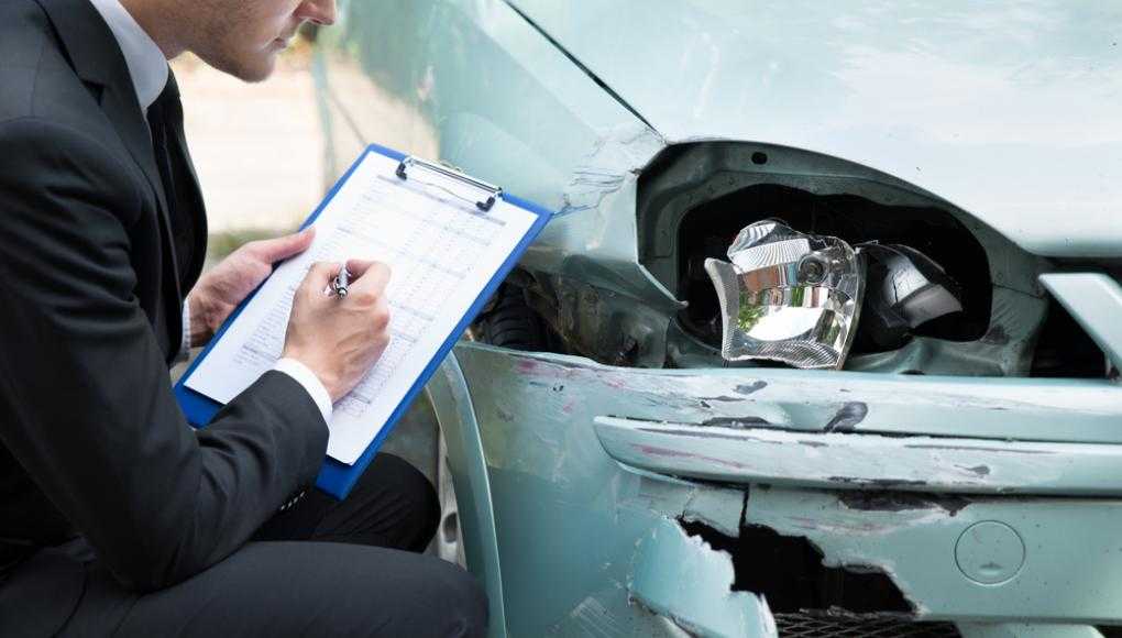 Insurance adjuster examining a damaged car and writing a report after a car accident