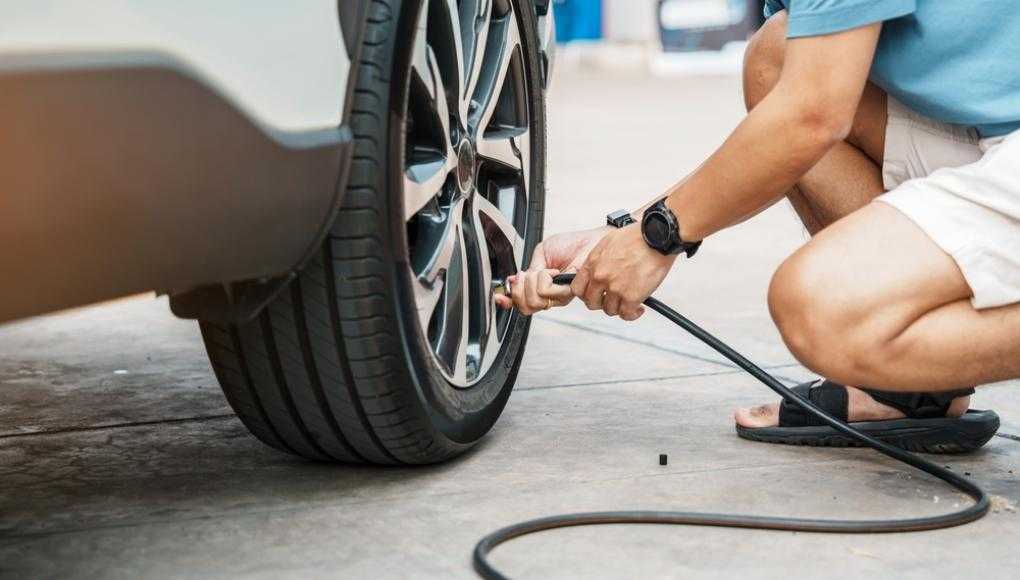 Person inflating a car tire with an air pump, ensuring proper tire maintenance and safety