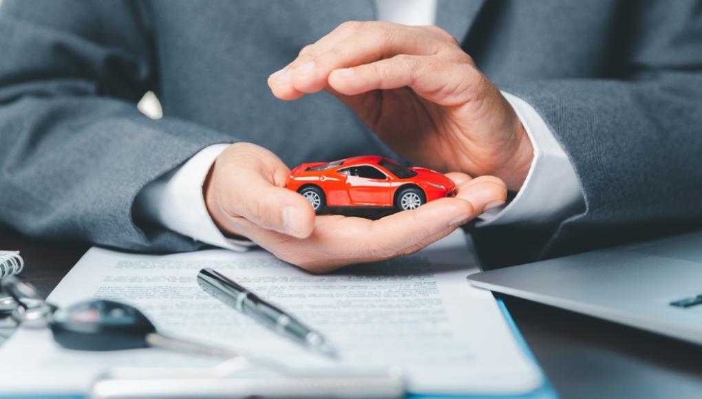 Insurance agent protecting a red toy car with hands, symbolizing car insurance and coverage consultation