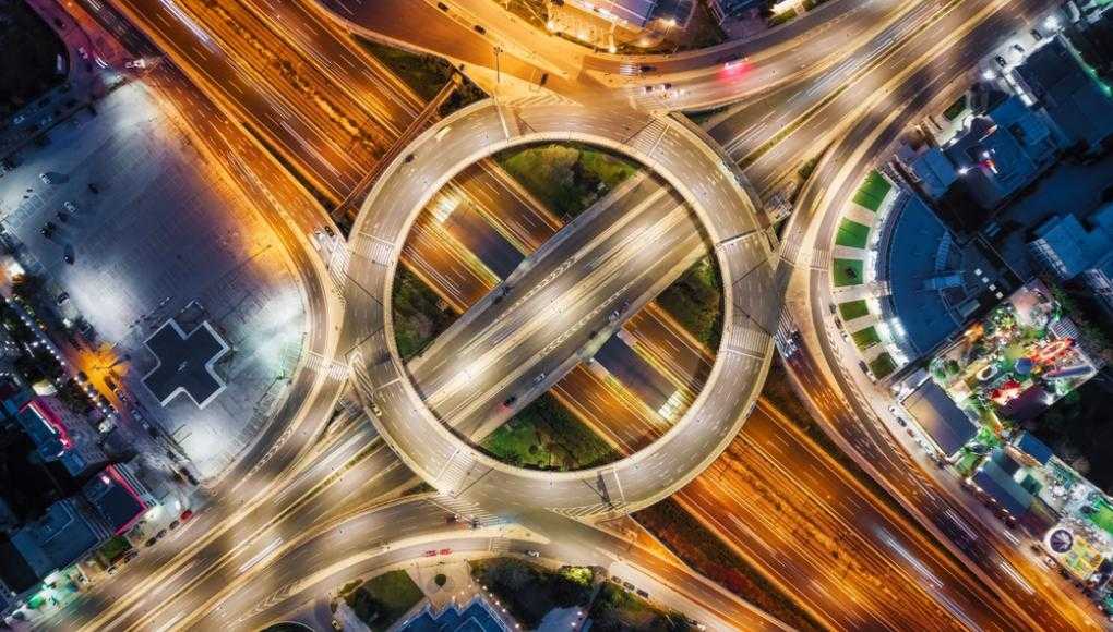 Aerial view of a busy roundabout with multiple intersecting highways at night, illustrating common car accident hotspots