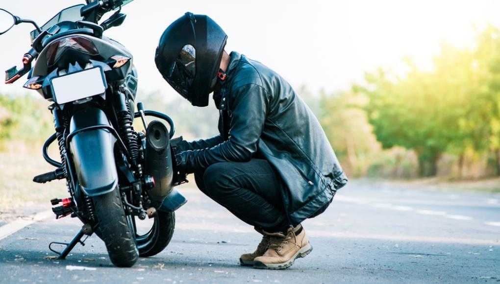 Motorcyclist in black leather gear and helmet inspecting their bike on the side of the road