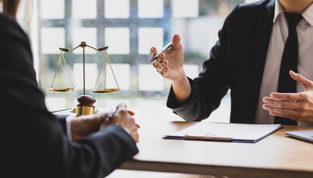 Lawyer explaining case details to a client in an office with a justice scale and gavel on the table.