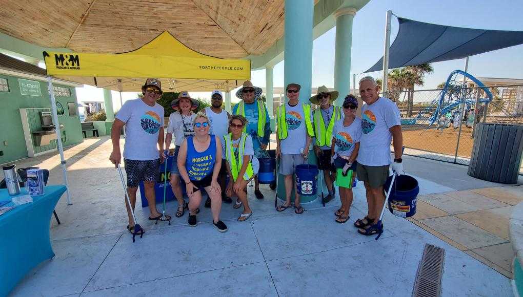 Group of volunteers from Morgan & Morgan participating in a beach and park cleanup event for World Oceans Day under a yellow M&M tent.