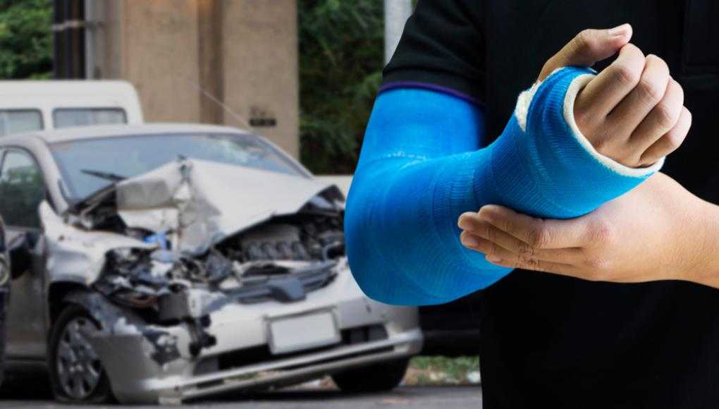 Man with an arm cast standing in front of a damaged car