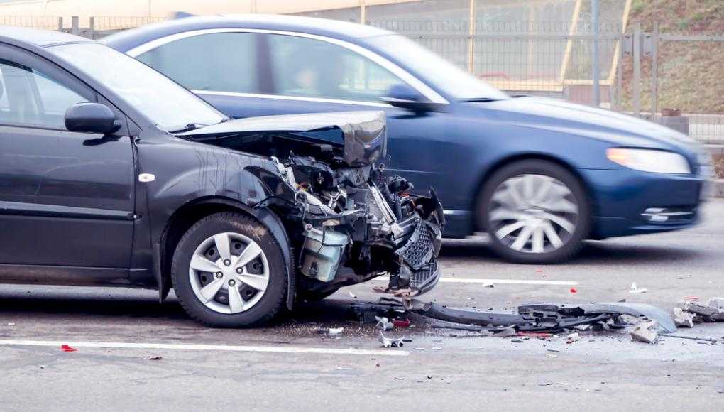 Car with lots of damage to its front end and another car driving by