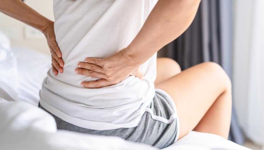 Women sitting on edge of bed holding back in pain 