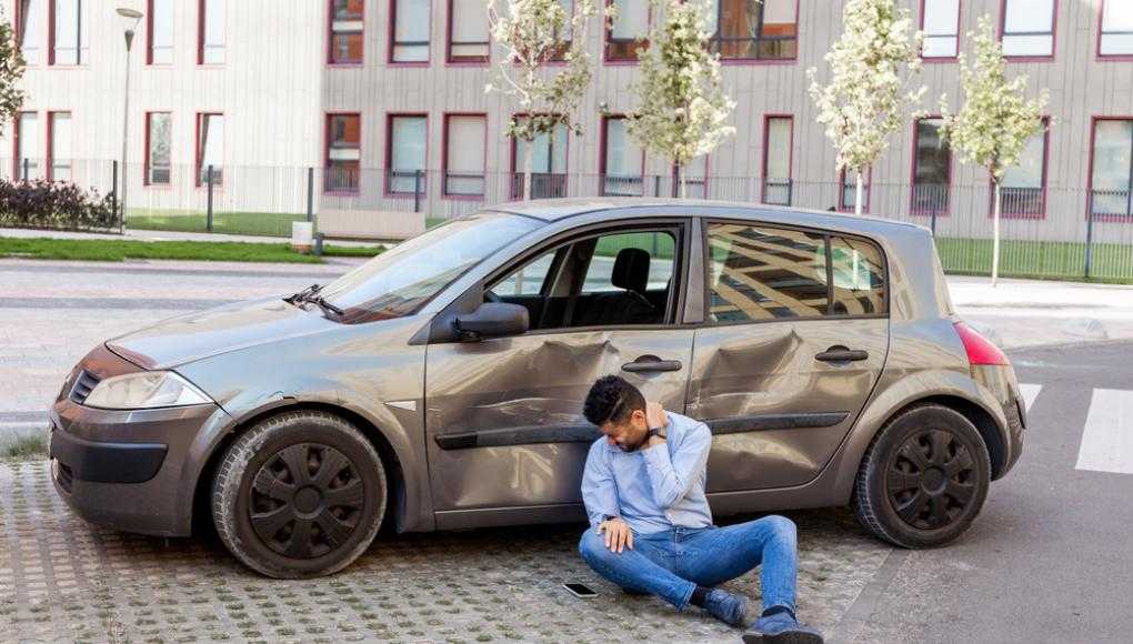 Man holding neck in pain next to damaged car