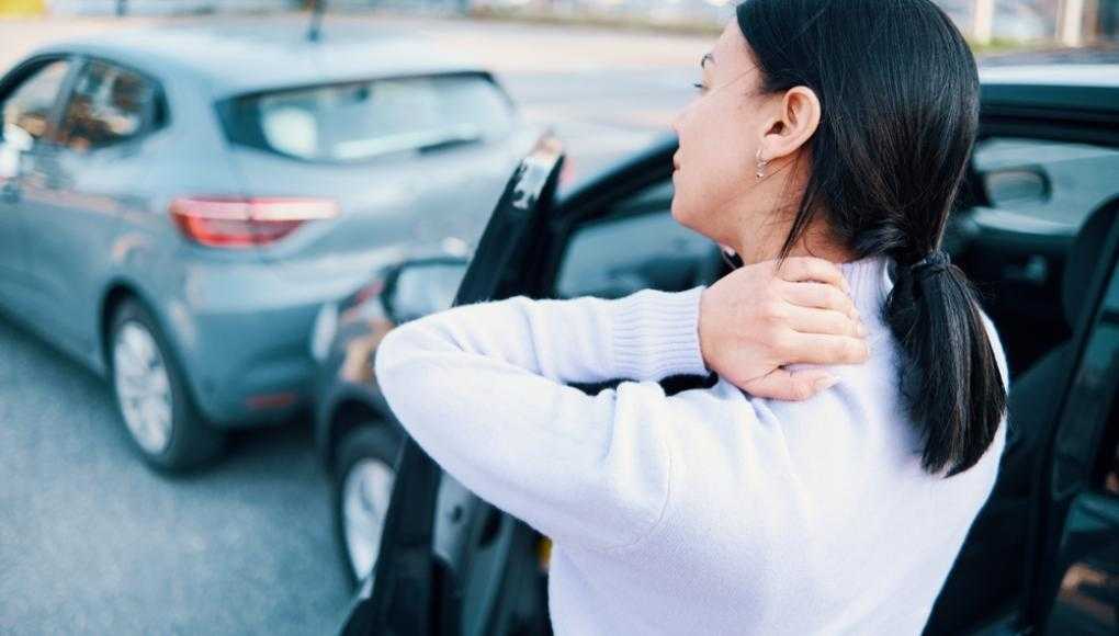 Woman holding her neck in pain standing outside of a car