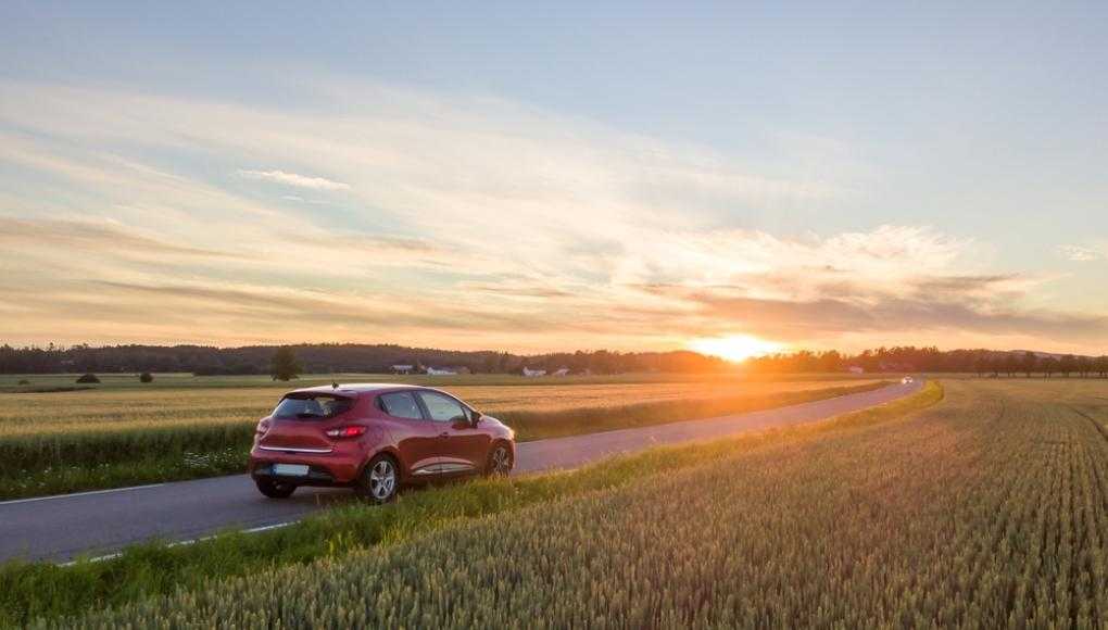 Car driving down a road with a sunset in the background