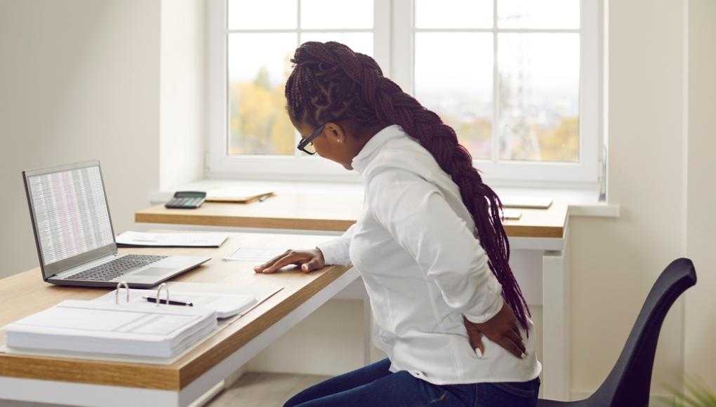 Woman at her desk holding back in pain