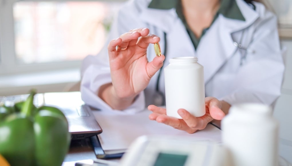 transparent yellow oval capsule and white jar in hand of Doctor nutritionist. food supplements, vitamin D, omega-3, fish oil