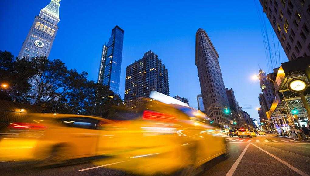 blurred yellow taxi speeding past historic Flatiron Building at dusk in New York City