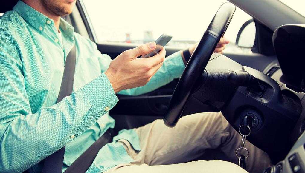 New Federal Guidelines Try to Get Drivers to Put Down Their Phones - A man driving a vehicle while using his mobile phone.
