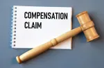 notepad with the words 'compensation claim' on it, with a grey background and wooden gavel resting on top of it