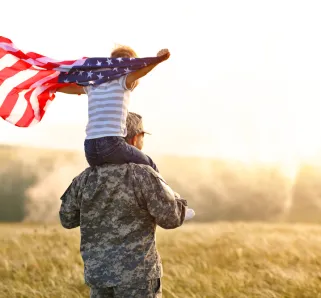 Rear view of military man father carrying happy little son with american flag on shoulders and enjoying amazing summer nature view on sunny day, happy male soldier dad reunited with son after US army