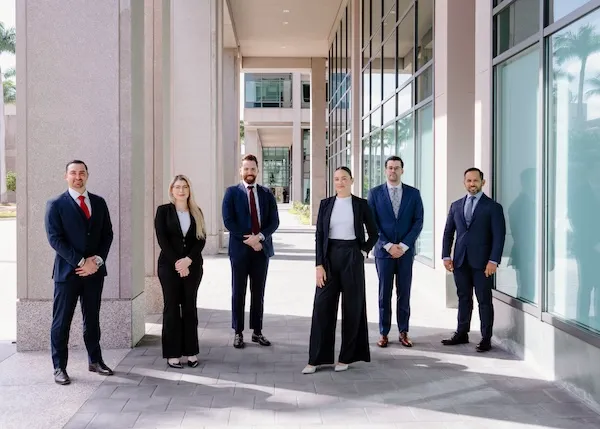 A group of six professionally dressed people stand outside a modern office building.