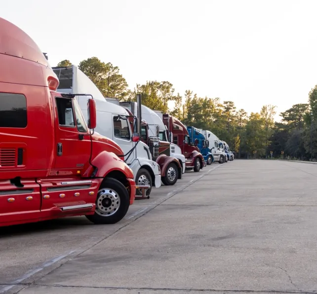 Row of colorful semi trucks lined up at dusk in a truck stop parking area.
