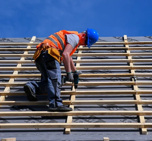 Repair and replacement of the old roof with a new one. Construction worker in protective clothing standing on roof with tools.