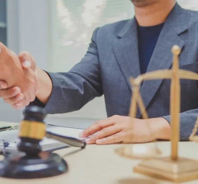 person shaking hands with lawyer with a scale and gavel on the desk