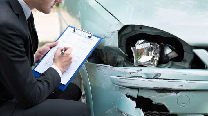 Insurance adjuster examining a damaged car and writing a report after a car accident