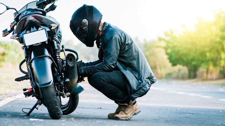 Motorcyclist in black leather gear and helmet inspecting their bike on the side of the road