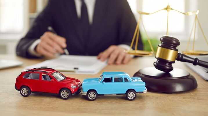 Car accident lawyer at a desk with toy cars, a gavel, and scales of justice in the foreground
