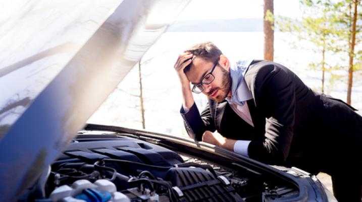 Stressed businessman looking at car engine breakdown