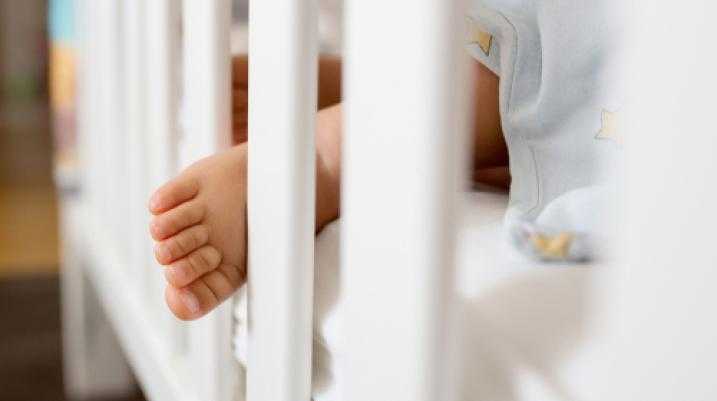 Close-up of a baby's foot sticking out between white crib slats