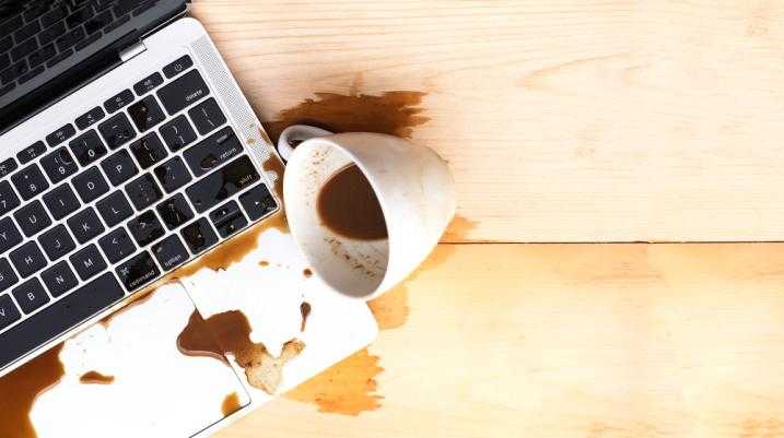 Spilled coffee on a laptop keyboard on a wooden desk