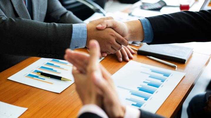 Business professionals shaking hands over a desk with financial charts, symbolizing agreement during the discovery process in legal proceedings