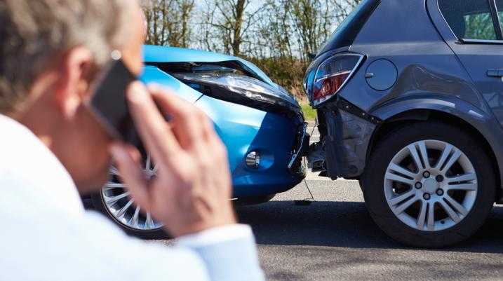 Man on phone after a car accident with visible damage to both cars.