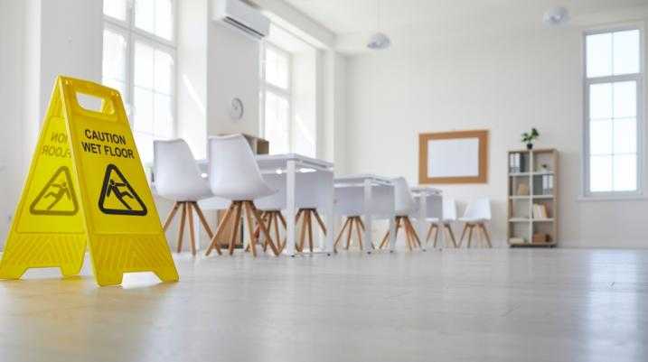 Yellow caution wet floor sign in spacious modern office with large windows and stylish furniture