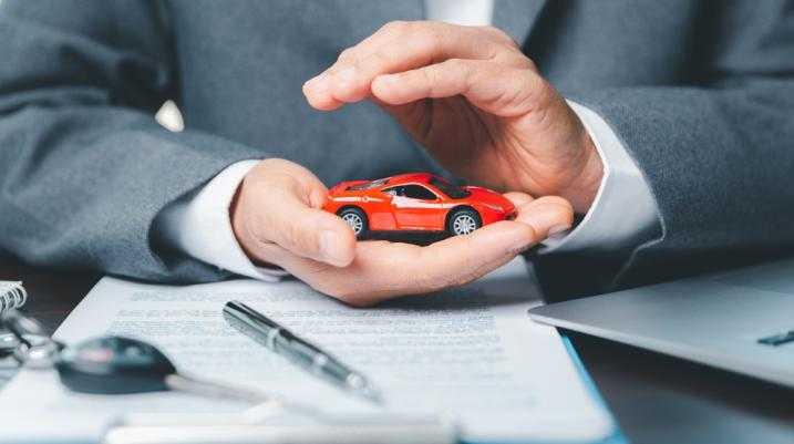 Insurance agent protecting a red toy car with hands, symbolizing car insurance and coverage consultation