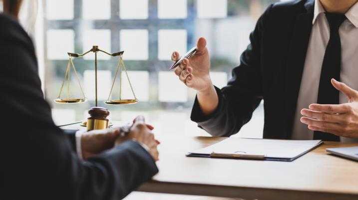 Lawyer explaining case details to a client in an office with a justice scale and gavel on the table.