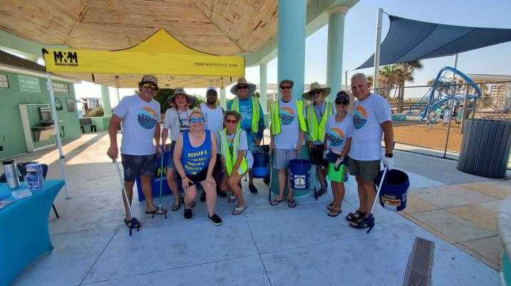 Group of volunteers from Morgan & Morgan participating in a beach and park cleanup event for World Oceans Day under a yellow M&M tent.