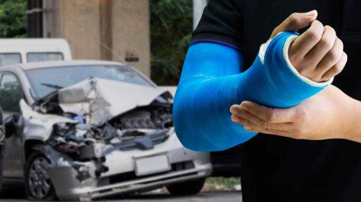 Man with an arm cast standing in front of a damaged car