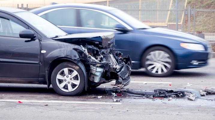 Car with lots of damage to its front end and another car driving by