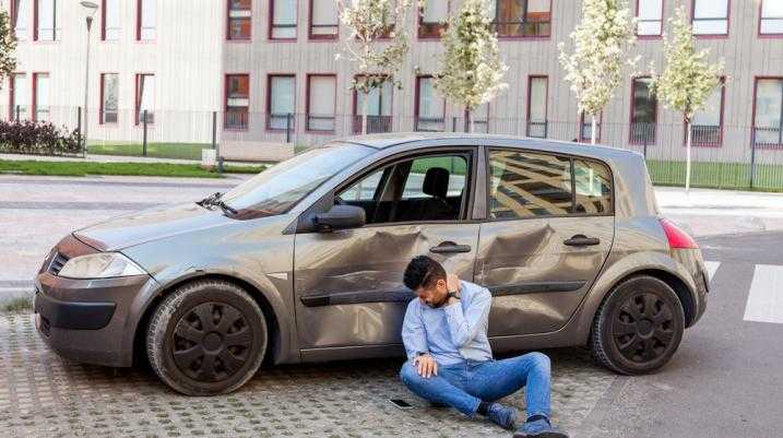 Man holding neck in pain next to damaged car