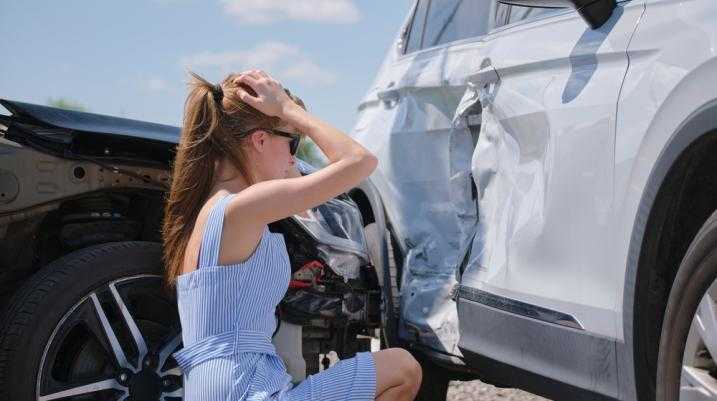 Woman in distress looking at her car after an accident